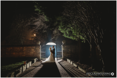 Couple embracing at night under gate's backlight.