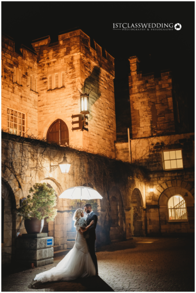 Couple embracing by lantern light at castle wedding.
