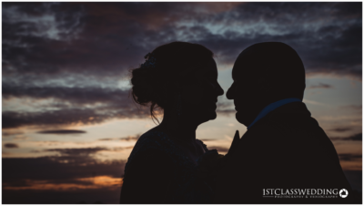 Couple silhouette against sunset sky at wedding.
