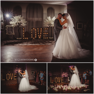 Bride and groom kissing at illuminated "LOVE" sign wedding.