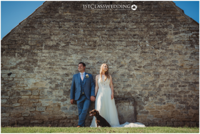 Bride, groom and dog by historic stone wall.