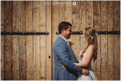 Bride and groom smiling by wooden barn doors.