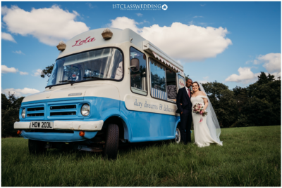 Bride and groom with vintage ice cream van in field.