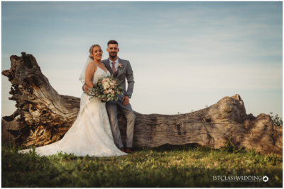 Bride and groom posing by a fallen tree outdoors.