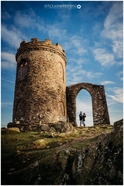 Couple posing at ancient tower ruins on hillside.