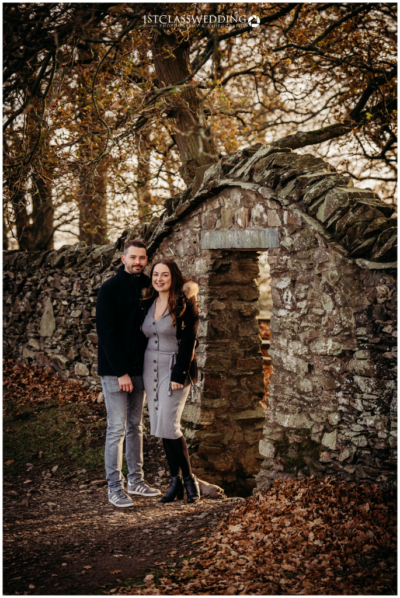 Couple posing by historic stone archway in autumn.