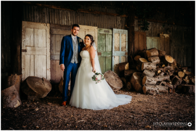 Wedding couple posing by rustic woodpile in barn.