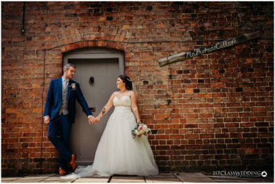 Bride and groom holding hands by brick wall.