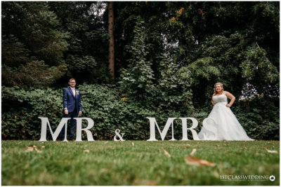 Bride and groom with 'MR & MRS' sign outdoors.