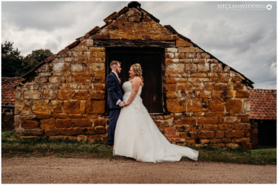 Bride and groom by rustic stone barn facade.