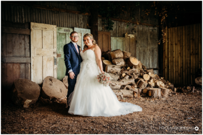 Bride and groom posing in rustic barn with logs.