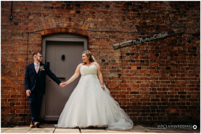 Bride and groom holding hands by brick wall.