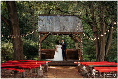 Outdoor wedding, couple under rustic arbor, fairy lights.