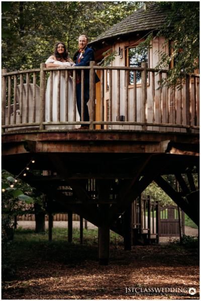 Couple on treehouse balcony in wedding attire.