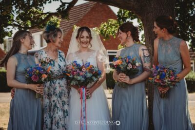Bride and bridesmaids with bouquets smiling outdoors.