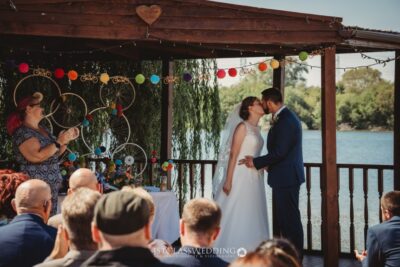 Couple kissing at lakeside wedding ceremony.