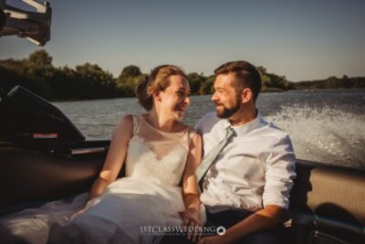 Newlyweds laughing on boat ride under sunny skies.