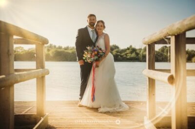 Couple embracing on pier, sunset, wedding attire.
