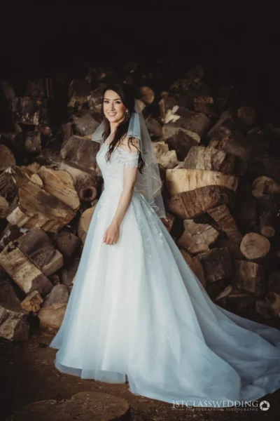 Bride in white dress smiling against firewood backdrop
