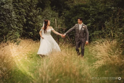 Bride and groom holding hands in meadow.