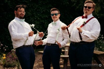 Three groomsmen posing with suspenders outdoors