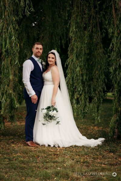 Bride and groom posing under willow tree.