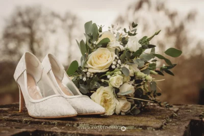 Bridal shoes with bouquet on stone wall.