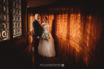 Couple in elegant wedding attire with warm lighting.