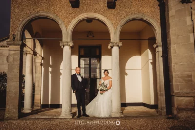 Elegant wedding couple posing by historical building columns.