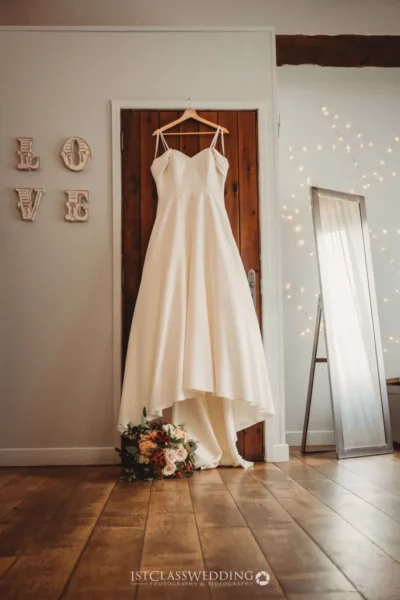 Wedding dress hanging near love sign and mirror.