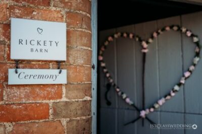 Rickety Barn ceremony sign with heart-shaped flower decoration.