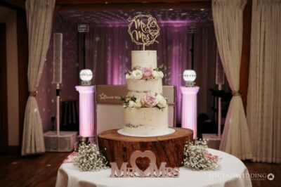 Elegant wedding cake on wooden stand with "Mr & Mrs" topper.