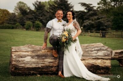 Happy couple posing on log at rustic wedding.