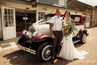 Wedding couple posing with vintage car on sunny day
