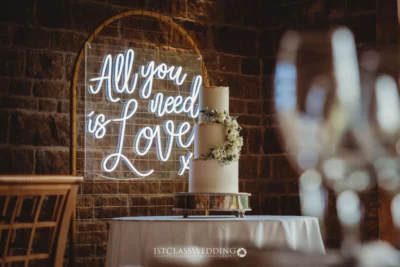 Wedding cake under neon 'All You Need is Love' sign.