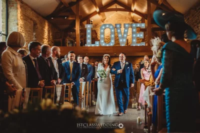 Bride walking aisle, "LOVE" sign, rustic wedding ceremony