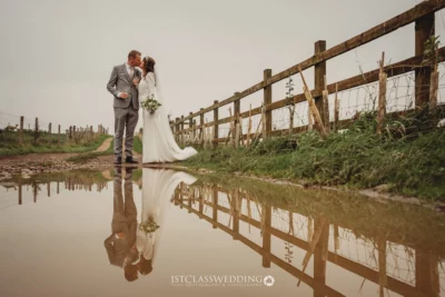 Couple kissing beside rural fence with reflection in water.