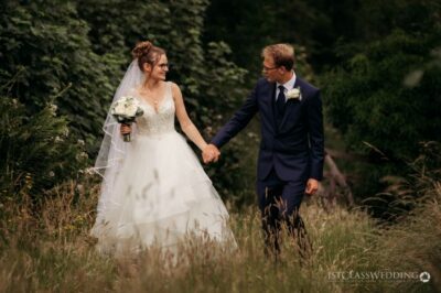 Bride and groom holding hands in nature.