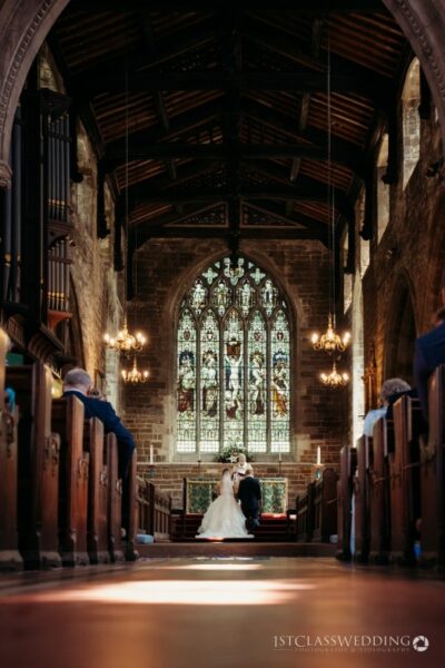 Bride and groom kissing in historical church aisle.