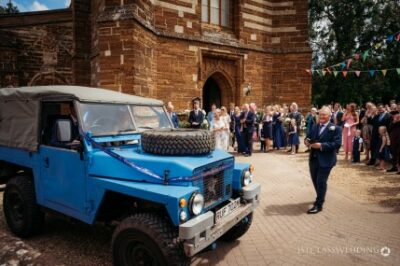 Wedding guests with Land Rover outside church.