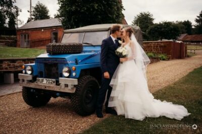 Couple kissing beside blue off-road vehicle at wedding.