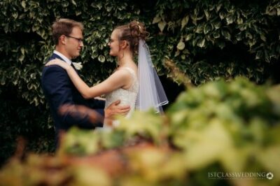 Bride and groom embracing at vine-covered outdoor wedding.