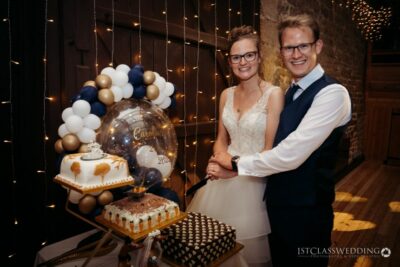 Couple with wedding cake in decorated venue.