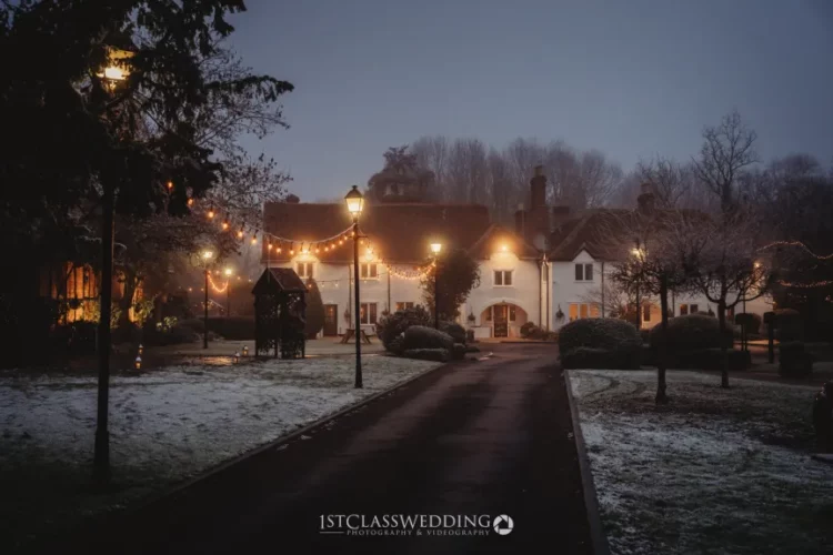 Twilight over snow-dusted manor with festive lights.