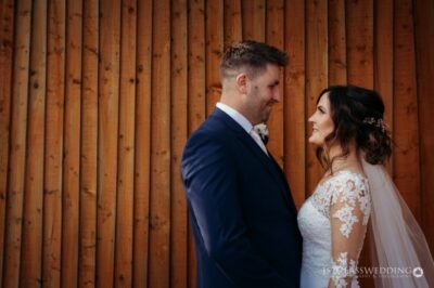Bride and groom smiling against wooden backdrop.
