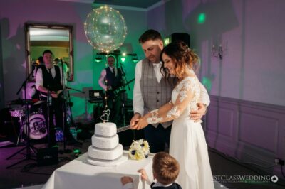 Bride and groom cutting wedding cake with live band background.