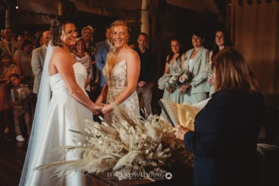 Joyful wedding ceremony with brides holding hands.