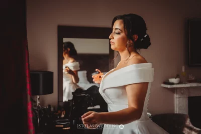Bride in white dress preparing with mirror reflection.