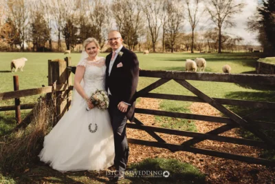 Bride and groom smiling in countryside with sheep.