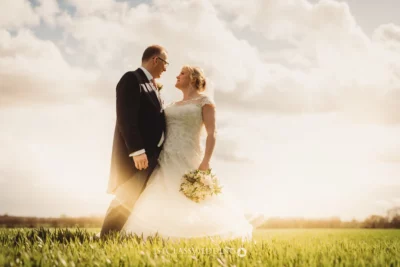 Couple in wedding attire outdoors with sunny backdrop